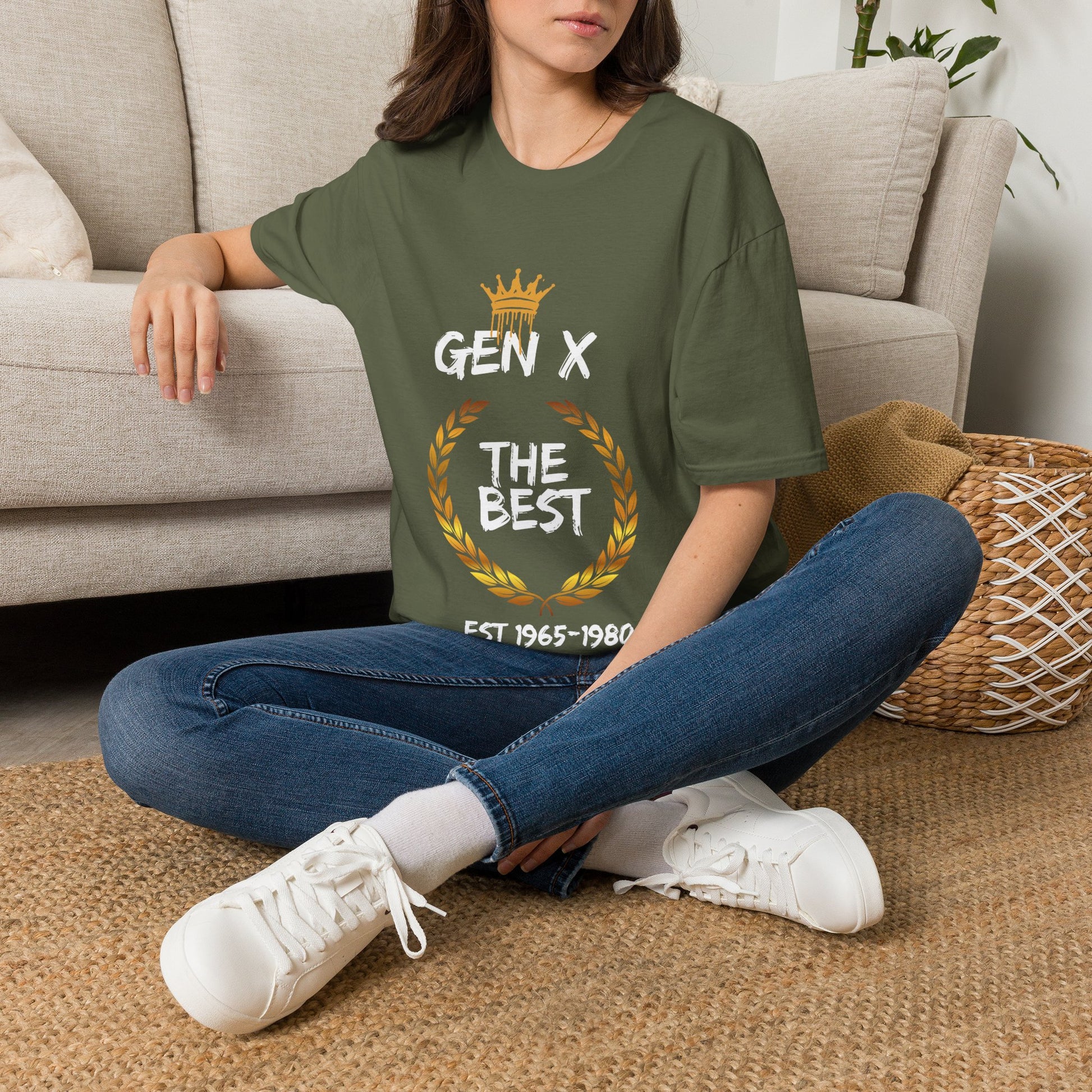 Person sitting on the floor in a living room wearing a green T-shirt with a gold crown and wreath graphic and white text saying Gen X The Best.