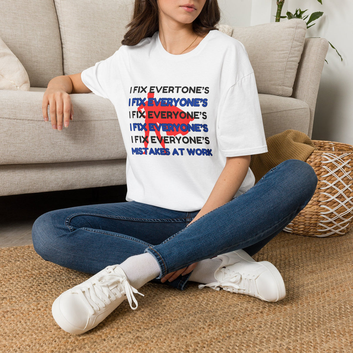 A white graphic t-shirt  featuring a text design that reads 'I FIX EVERYONE'S MISTAKES AT WORK' with a red scribble over repeated 'I FIX EVERYONE'S' lines. 