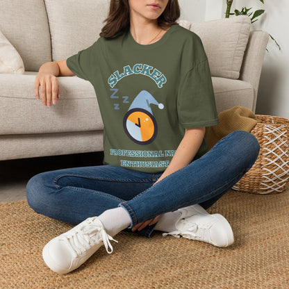 A woman sitting on a woven rug in front of a beige couch, wearing an green graphic t-shirt with a 'Slacker professional nap enthusiast' clock graphic, blue jeans, and white sneakers.