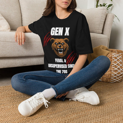 A woman sitting cross-legged on a woven rug in front of a beige sofa, wearing a black graphic T-shirt with a bear illustration and the text 'GEN X FERAL & UNSUPERVISED SINCE THE 70S'.