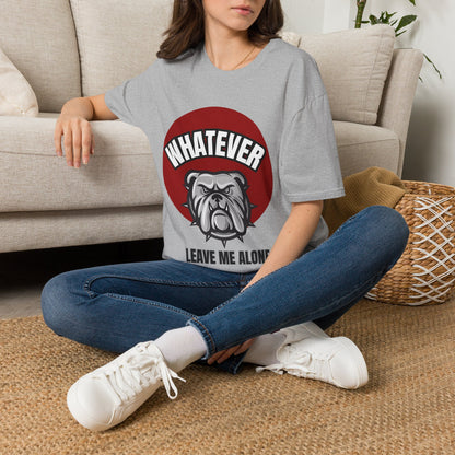 A woman sitting cross-legged on a woven rug in front of a beige sofa, wearing a gray graphic t-shirt with a red circle, white text reading 'WHATEVER', and a bulldog illustration, paired with blue jeans and white sneakers.