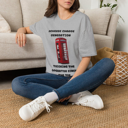 A woman sitting cross-legged on a woven rug in front of a beige sofa, wearing a gray graphic T-shirt with a red telephone booth print and text, blue jeans, and white sneakers.