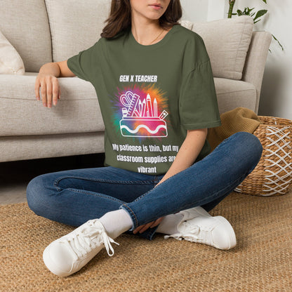 A woman sitting cross-legged on a woven rug in front of a beige sofa, wearing an green graphic T-shirt with a colorful school supplies design and the text 'GEN X TEACHER' and 'My patience is thin, but my classroom supplies are vibrant'.