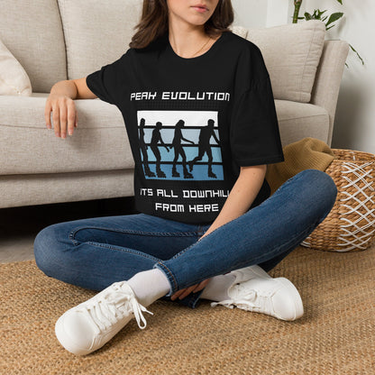 A woman sitting cross-legged on a woven rug in front of a beige sofa, wearing a black graphic T-shirt with the text 'PEAK EVOLUTION IT'S ALL DOWNHILL FROM HERE' and a white, blue, and black boxing-ring graphic.