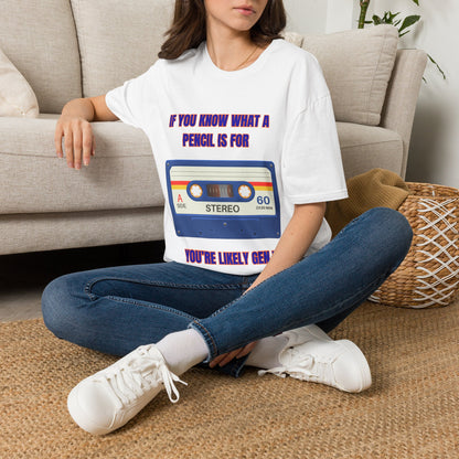A woman sitting on a woven rug in front of a beige couch, wearing a white graphic t-shirt with a retro cassette tape design with the text "IF YOU KNOW WHAT A PENCIL IS FOR YOU'RE LIKELY GEN X" and blue jeans.