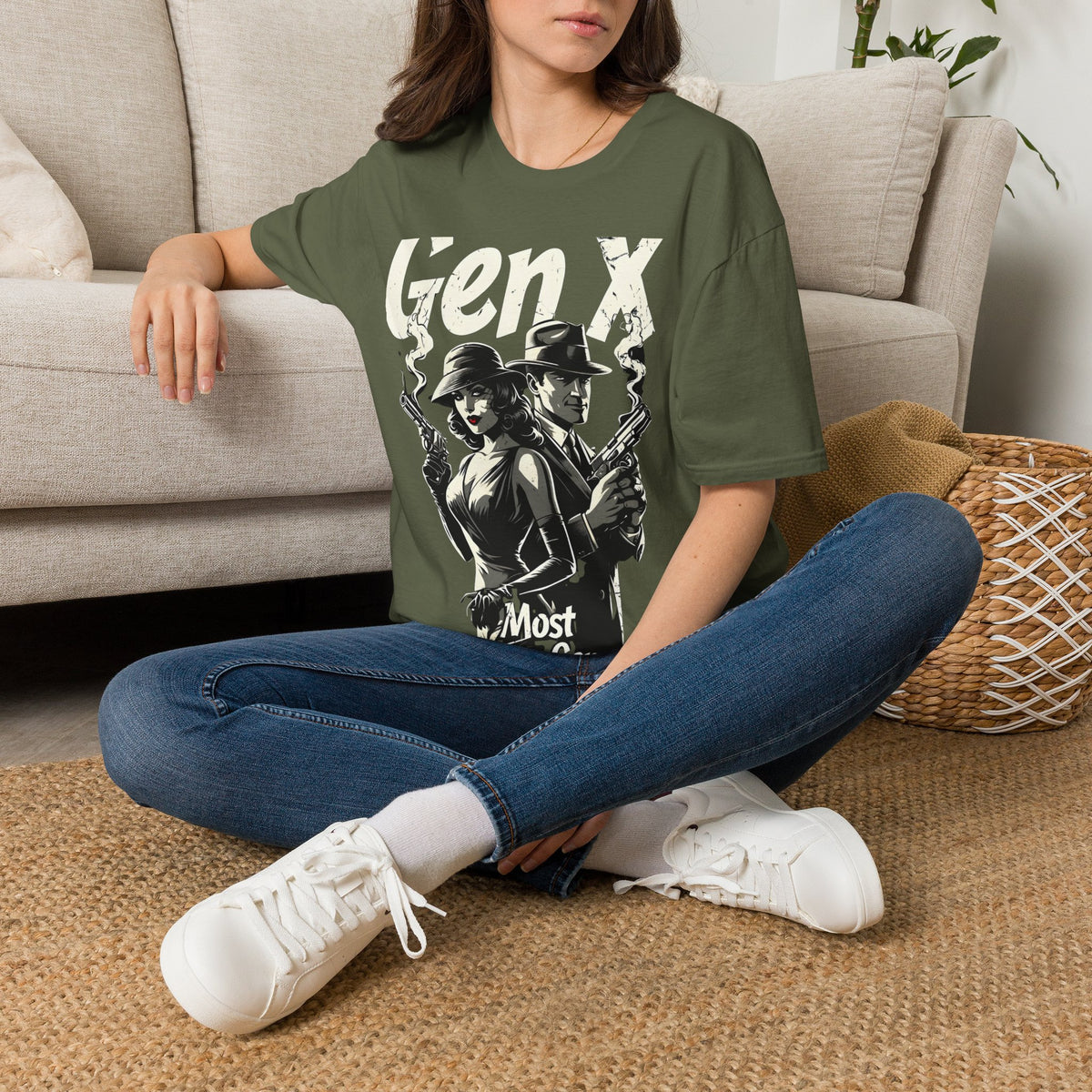 A woman sitting on a rug on the floor next to a couch wearing a green t-shirt with a graphic of a man and woman standing back to back holding smoking guns and the text "GEN X MOST DANGEROUS GENERATION" 