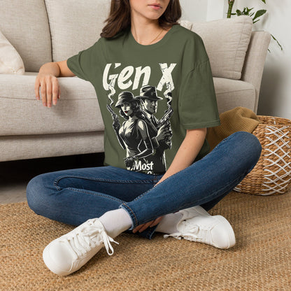 A woman sitting on a rug on the floor next to a couch wearing a green t-shirt with a graphic of a man and woman standing back to back holding smoking guns and the text "GEN X MOST DANGEROUS GENERATION" 