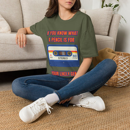 A woman sitting on a woven rug in front of a beige couch, wearing a green graphic t-shirt with a retro cassette tape design and red text that reads 'IF YOU KNOW WHAT A PENCIL IS FOR YOUR LIKELY GENIUS'.