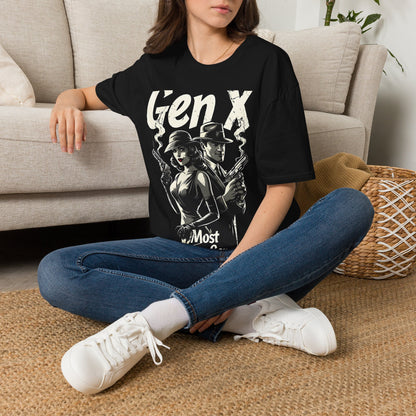 A woman stting on a rug on the floor next to a beige couch wearing a black t-shirt with a graphic of a man and woman standing back to back holding smoking guns with the text "GEN X MOST DANGEROUS GENERATION" wearing jeans and white sneakers.