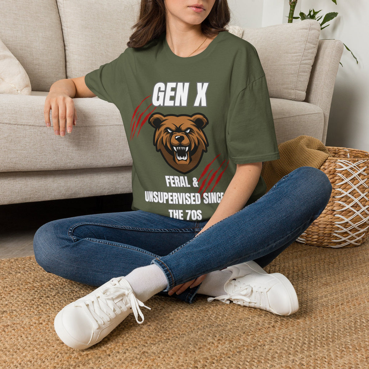 A woman sitting cross-legged on a woven rug in front of a beige sofa, wearing a green graphic T-shirt with a bear illustration and the text 'GEN X FERAL & UNSUPERVISED SINCE THE 70S'.