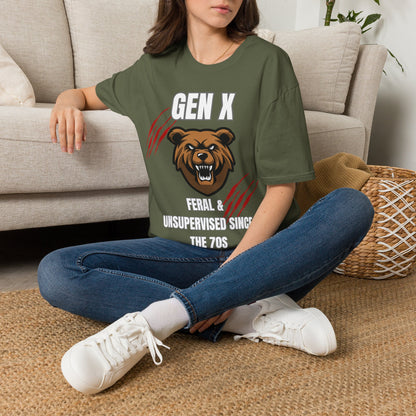 A woman sitting cross-legged on a woven rug in front of a beige sofa, wearing a green graphic T-shirt with a bear illustration and the text 'GEN X FERAL & UNSUPERVISED SINCE THE 70S'.