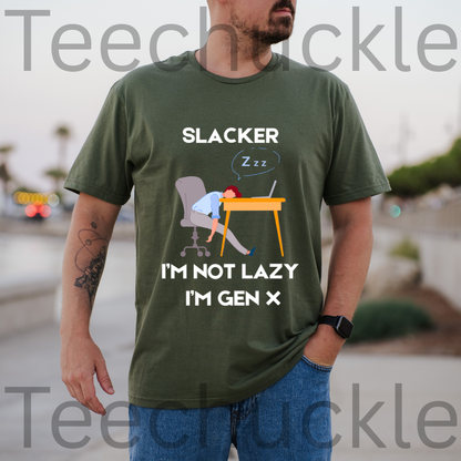 A man wearing a green graphic t-shirt with a 'Slacker, IM NOT LAZY IM GEN X' cartoon illustration of a man sleeping at a desk paired with blue jeans, set against a blurred outdoor background 