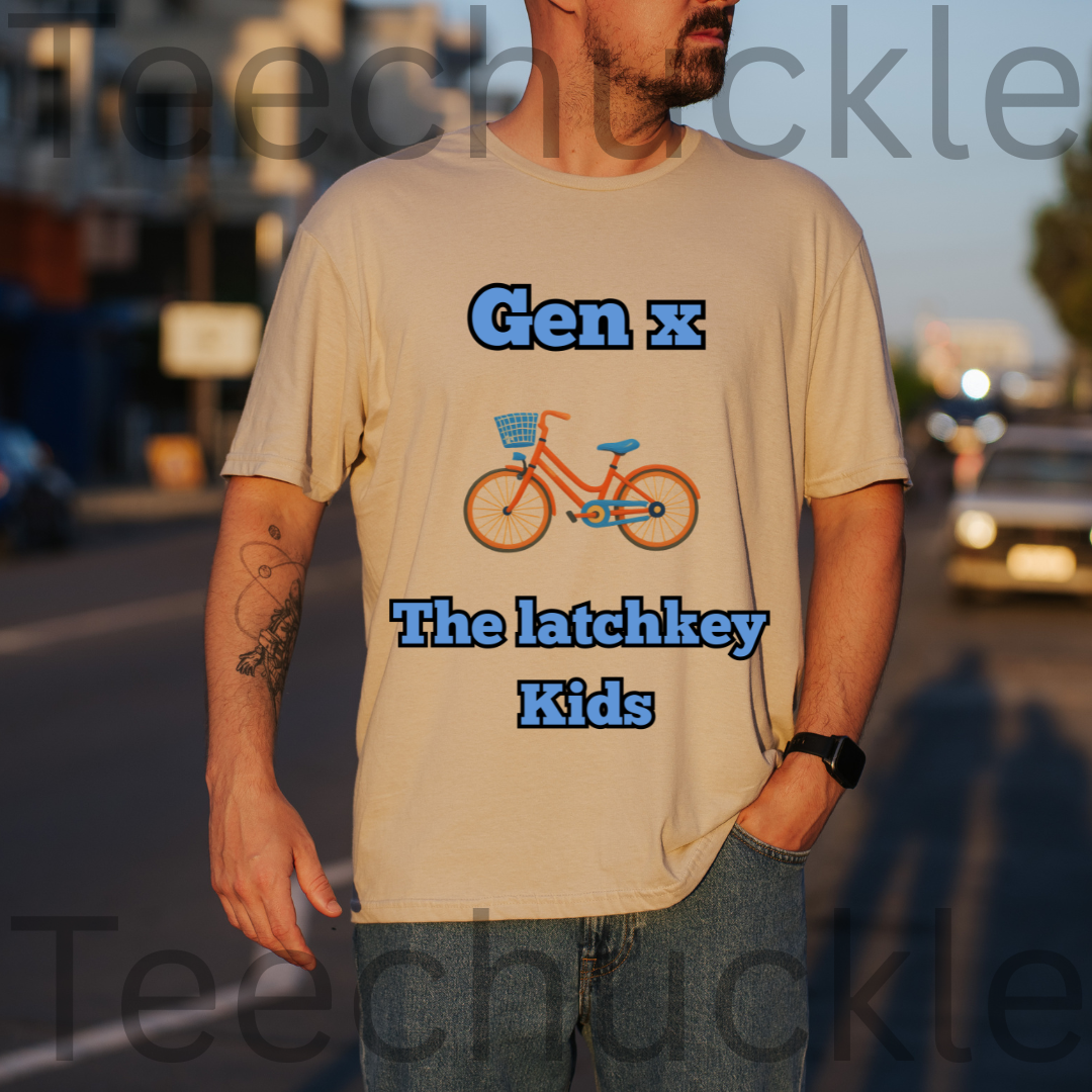 A man wearing a sand graphic t-shirt with a blue bicycle illustration and the text 'Gen x The latchkey Kids' in blue, standing outdoors on a street at sunset.