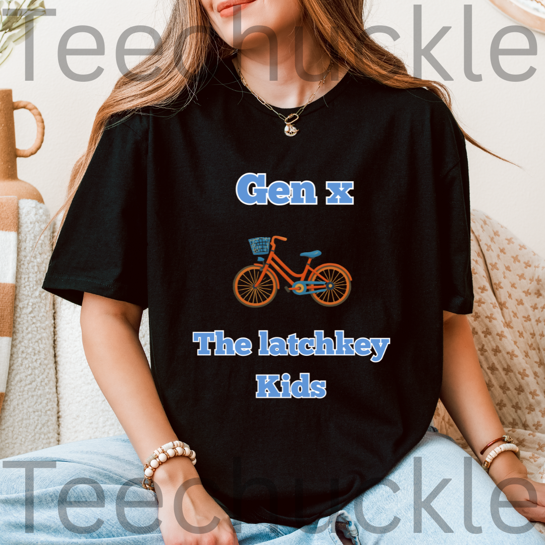 A woman wearing a black graphic t-shirt with the text 'Gen X The latchkey Kids' in blue and an illustration of an orange bicycle. The photo is taken in a cozy indoor setting with a beige couch and a wooden vase in the background.
