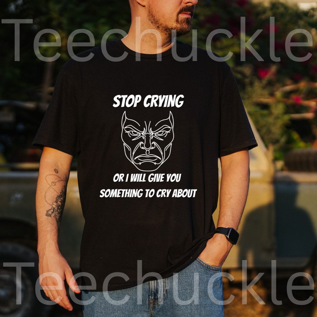 A man wearing a black graphic t-shirt with a white line art design and the text 'STOP CRYING OR I WILL GIVE YOU SOMETHING TO CRY ABOUT'. The background is an outdoor setting with a blurred truck and foliage.