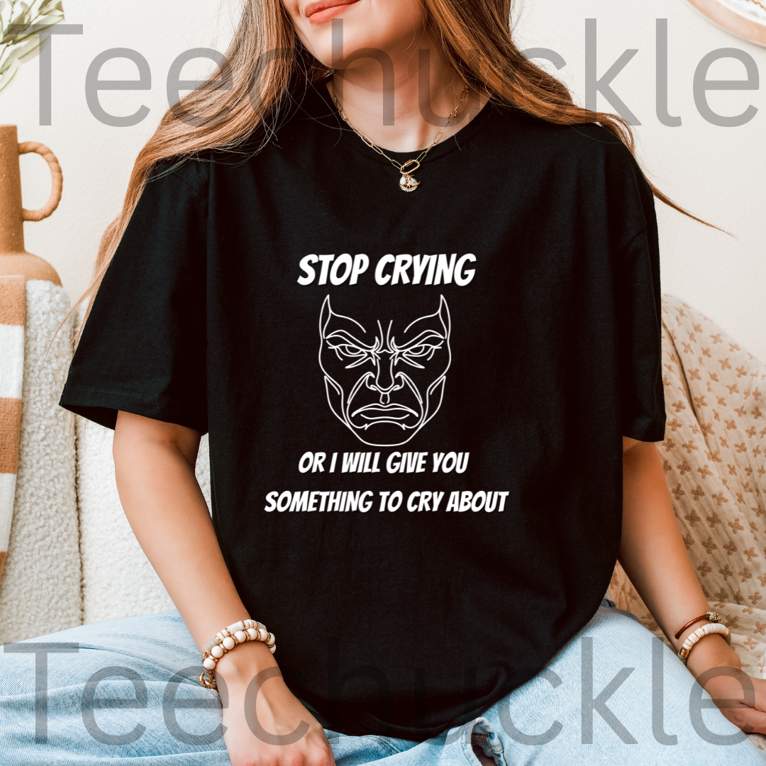 A woman wearing a black graphic t-shirt with a white printed design that reads 'STOP CRYING OR I WILL GIVE YOU SOMETHING TO CRY ABOUT' alongside a stylized angry face illustration. The image has a prominent 'Teechuckle' watermark overlay.