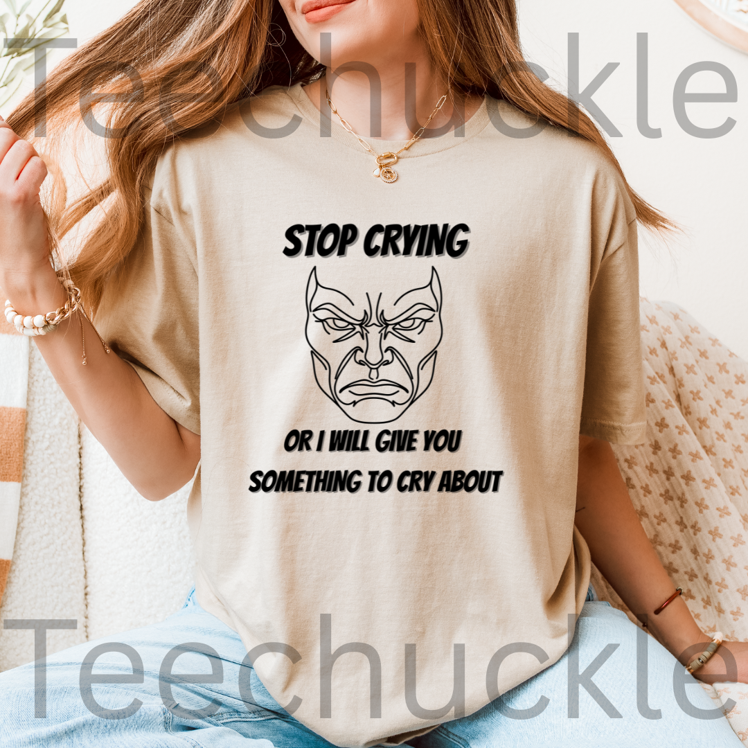A woman wearing a sand graphic t-shirt with a black printed face and the text 'STOP CRYING OR I WILL GIVE YOU SOMETHING TO CRY ABOUT'.