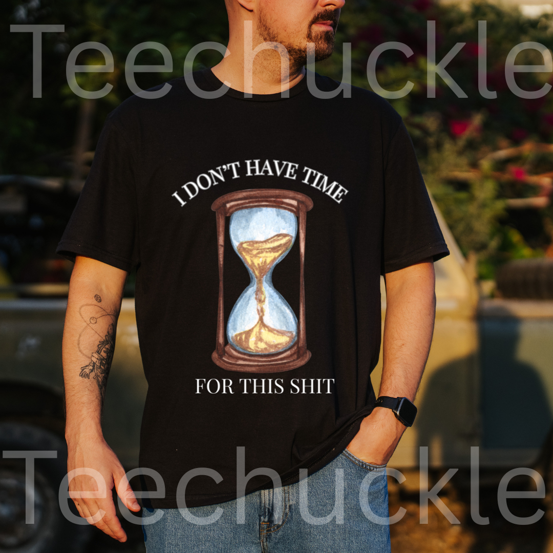 A man wearing a black graphic t-shirt with a humorous text "I DON'T HAVE TIME FOR THIS SHIT" design and an hourglass illustration, set against an outdoor background 