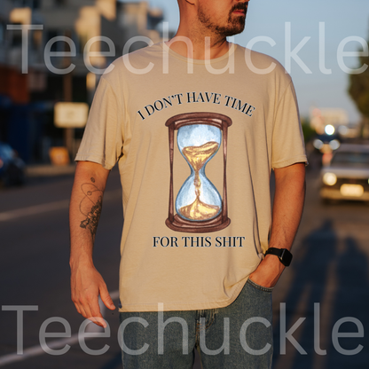 A man wearing a sand graphic t-shirt with a printed hourglass design and the text 'I DON'T HAVE TIME FOR THIS SHIT'. The photo is taken outdoors in warm evening light with a blurred street background