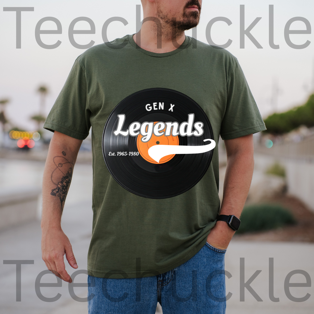 A man wearing an olive green t-shirt with a 'Gen X Legends' vinyl record graphic on the front, set against a blurred outdoor background. 