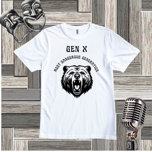 A white short-sleeve t-shirt with a black graphic print featuring a roaring bear and the text 'GEN X MOST DANGEROUS GENERATION'. The shirt is displayed flat on a gray wood panel background with vintage-style props (a metal microphone and a silver mask) in the corners.