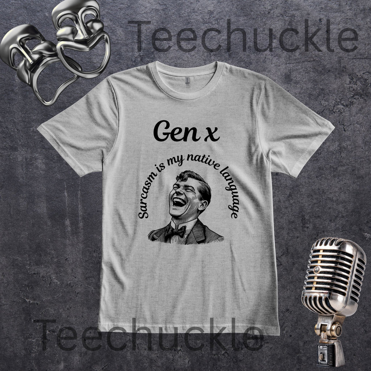 A gray crewneck t-shirt with a black graphic print featuring the text 'Gen x' and 'Sarcasm is my native language' around a laughing man's portrait. The shirt is displayed on a textured dark gray background with vintage microphone and theater mask props