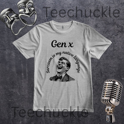 A gray crewneck t-shirt with a black graphic print featuring the text 'Gen x' and 'Sarcasm is my native language' around a laughing man's portrait. The shirt is displayed on a textured dark gray background with vintage microphone and theater mask props