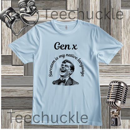 A light blue short-sleeve graphic t-shirt featuring a black illustration of a laughing man with the text 'Gen x' and 'Sarcasm is my native language' printed on the front. The shirt is displayed on a rustic wood plank background with vintage microphone and theater prop graphics