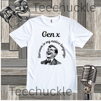 A white short-sleeve graphic T-shirt laid flat on a wood plank background, with black text reading 'Gen x' and 'Sarcasm is my native language' around a black-and-white portrait illustration. Decorative vintage theater masks and a retro microphone appear around the shirt