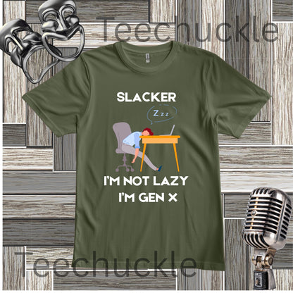 A green graphic t-shirt featuring a cartoon illustration of a person sleeping at a desk with the text 'SLACKER I'M NOT LAZY I'M GEN X'. The t-shirt is displayed on a gray wood-plank background with vintage-style microphones