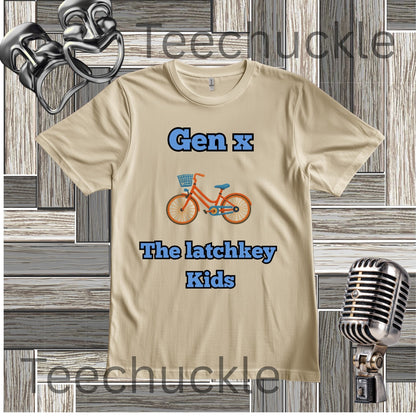 A sand graphic t-shirt featuring the text 'Gen x' and 'The latchkey Kids' in blue, with an orange bicycle illustration in the center. The t-shirt is displayed on a gray wood-plank background with vintage microphone props and a comedy masks