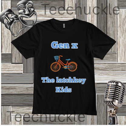 A black short-sleeve graphic t-shirt featuring the text 'Gen x The latchkey Kids' in blue, with an orange and blue bicycle illustration in the center. The t-shirt is displayed on a gray wood-paneled background with decorative props including a silver microphone and theatrical masks