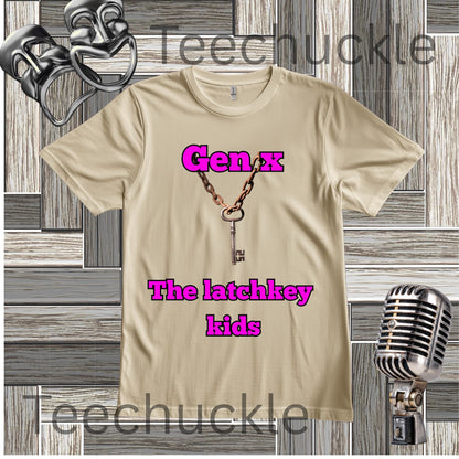A sand graphic t-shirt featuring a key necklace design and the text 'Gen x The latchkey kids' in pink, displayed on a gray wood plank background with vintage microphone and headphones props. 