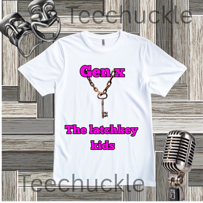 A white short-sleeve graphic t-shirt featuring a vintage key necklace design with the text 'Gen X The latchkey kids' in pink. The shirt is displayed on a gray wood-paneled background with vintage microphone and comedy mask props.