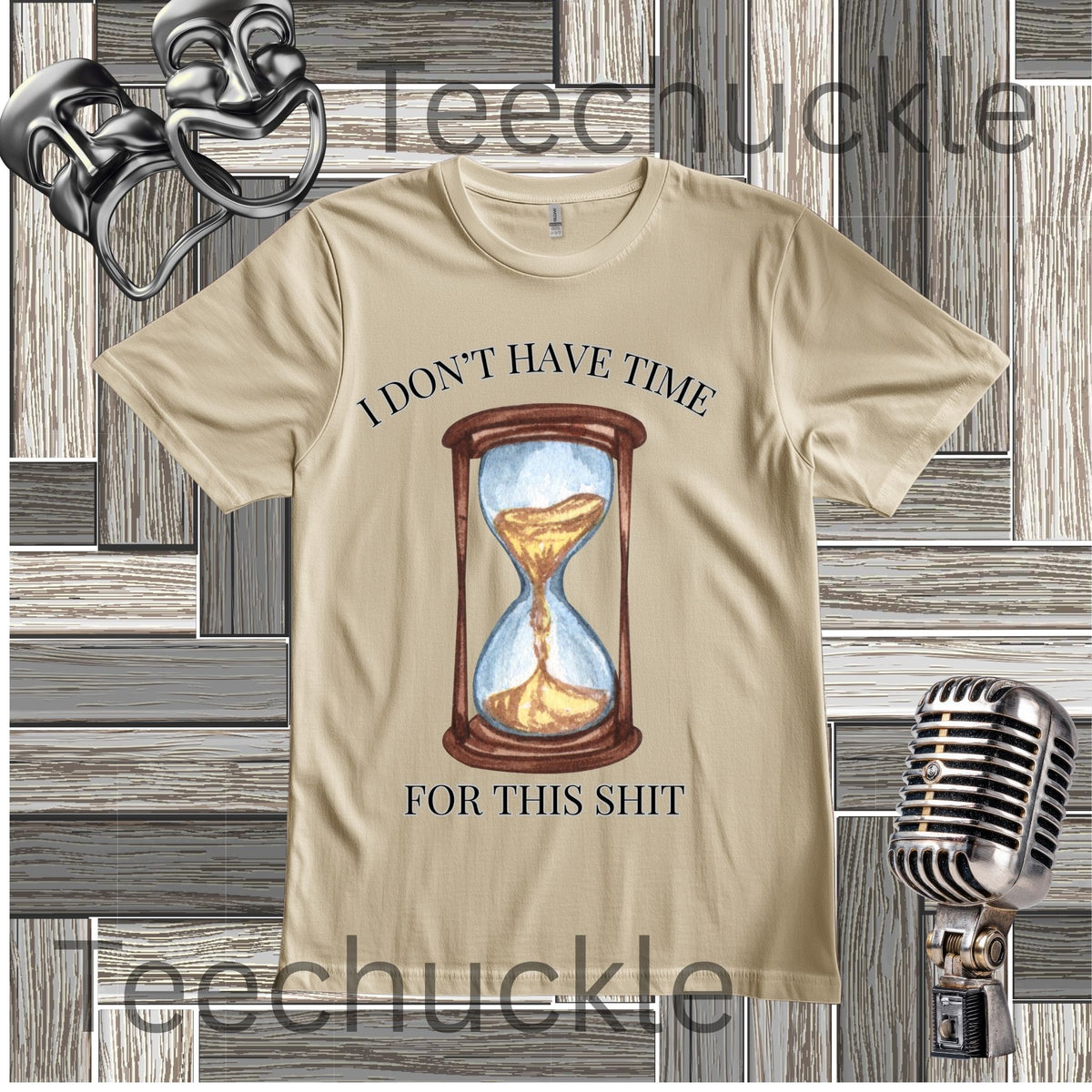 A sand graphic t-shirt featuring a printed illustration of an hourglass with sand flowing through, and the text 'I DON'T HAVE TIME FOR THIS SHIT' in black. The t-shirt is displayed on a gray wood-plank background with vintage microphone props