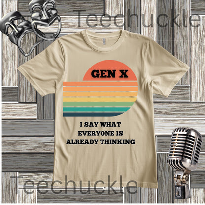 A sand graphic t-shirt featuring a retro sunset design with the text 'GEN X' and 'I SAY WHAT EVERYONE IS ALREADY THINKING' in black. The t-shirt is displayed on a gray wood panel background with vintage microphone and headphones props