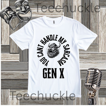 A white short-sleeve graphic t-shirt with a black circular print featuring a roaring viking man and the text 'YOU CAN'T HANDLE MY SARCASM GEN X'. The shirt is displayed on a rustic wood panel background with vintage-style props, including a silver microphone and a comedy mask