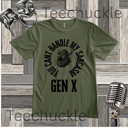 A green graphic t-shirt featuring a black circular design with a horned creature and the text 'YOU CAN'T HANDLE MY SARCASM GEN X'. The t-shirt is displayed on a gray wood panel background with vintage-style props, including a silver microphone and a comedy masks, 