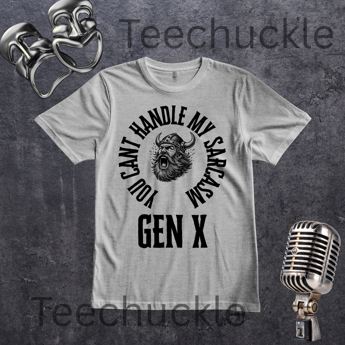 A grey short-sleeve graphic t-shirt with a black circular print featuring a roaring viking man and the text 'YOU CAN'T HANDLE MY SARCASM GEN X'. The shirt is displayed on a rustic wood panel background with vintage-style props, including a silver microphone and a comedy mask