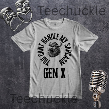 A grey short-sleeve graphic t-shirt with a black circular print featuring a roaring viking man and the text 'YOU CAN'T HANDLE MY SARCASM GEN X'. The shirt is displayed on a rustic wood panel background with vintage-style props, including a silver microphone and a comedy mask