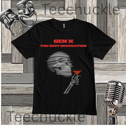 A black short-sleeve graphic T-shirt laid flat on a wood plank background, featuring red text reading 'GEN X THE BEST GENERATION' above a gray illustrated figure holding a red martini glass. Decorative props including a mask, vintage microphone, and theatrical masks appear around the shirt
