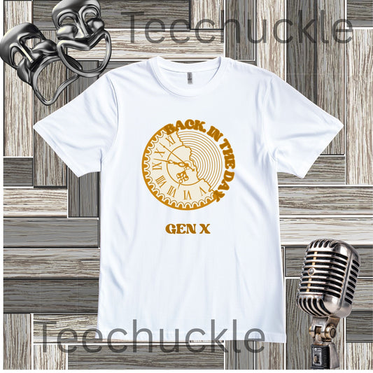 A white short-sleeve graphic t-shirt featuring a circular gold clock with 'Back in the Day GEN X' text around it design, displayed on a gray wood panel background with vintage microphone and comedy mask props.