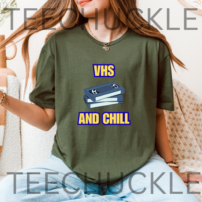 A woman wearing an oversized green graphic t-shirt with a VHS tape illustration and the text 'VHS AND CHILL' in yellow and blue. 
