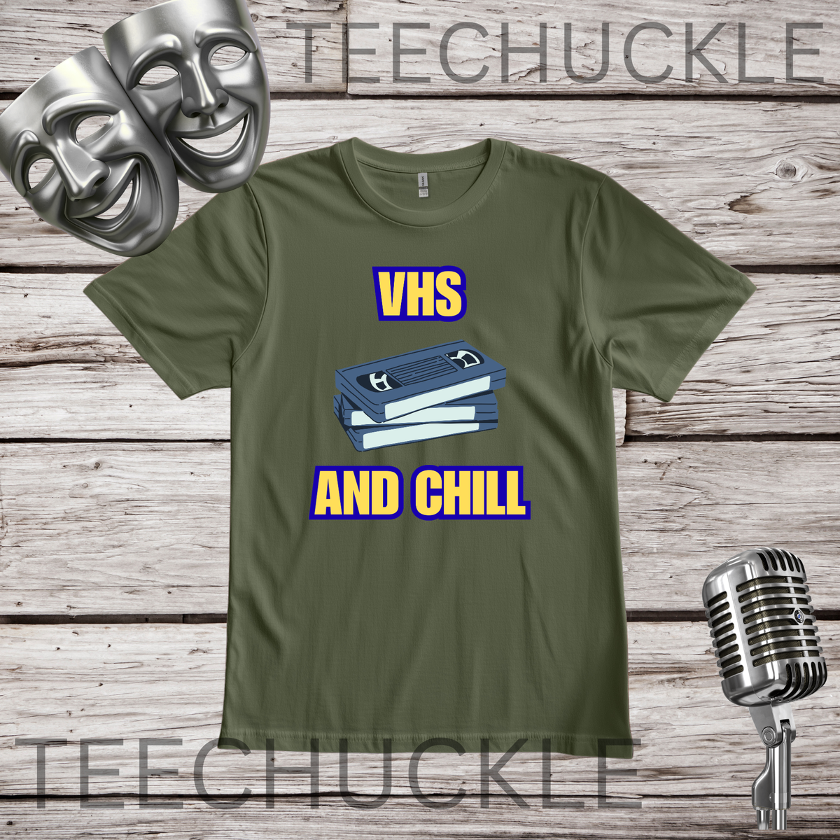 A green graphic t-shirt featuring a blue VHS tape illustration with the text 'VHS AND CHILL' in yellow with a blue outline. The t-shirt is displayed on a rustic wooden background with silver comedy and comedy masks, a vintage microphone.