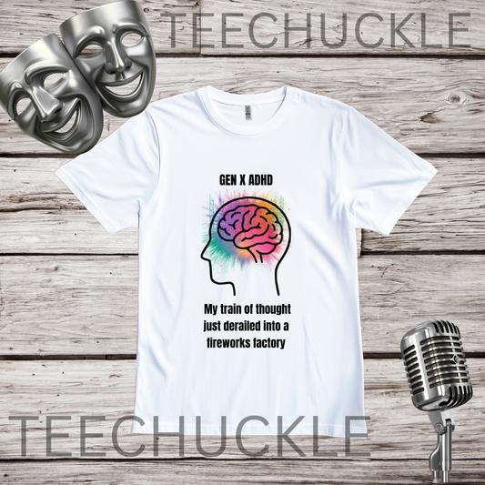 A white short-sleeve graphic T-shirt laid flat on a rustic wood plank background, with two silver comedy masks in the upper left and a vintage microphone in the lower right. The shirt has a colorful brain silhouette graphic and black text reading 'GEN X ADHD My train of thought just derailed into a fireworks factory.