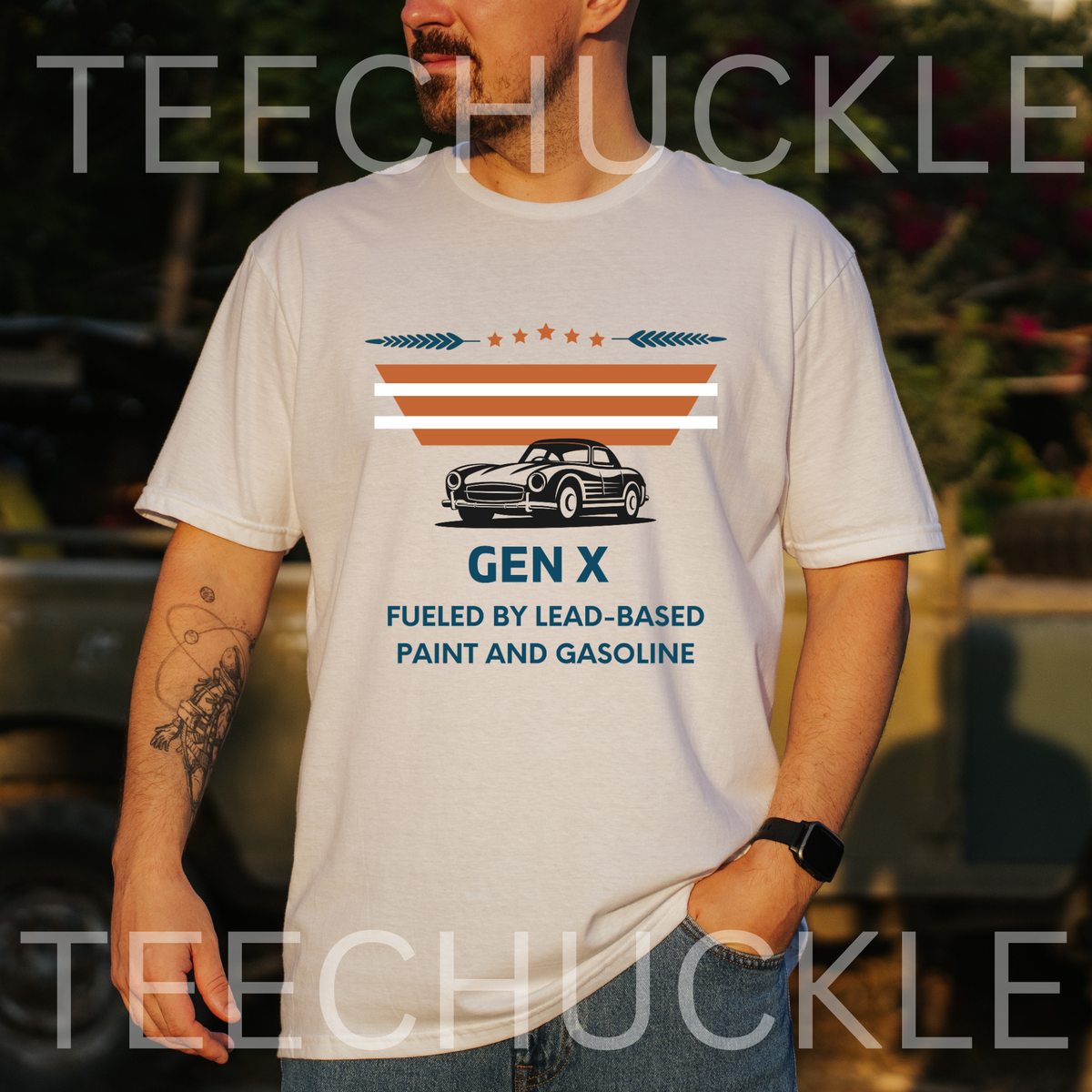 A man standing outside wearing a white graphic t-shirt displayed. The t-shirt features a retro design with the text 'GEN X FUELED BY LEAD-BASED PAINT AND GASOLINE' and an illustration of a classic car under orange and white stripes.