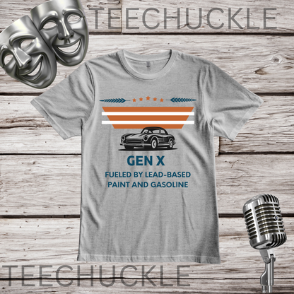 A gray graphic t-shirt displayed flat on a rustic wood background, featuring a vintage car illustration and the text 'GEN X FUELED BY LEAD-BASED PAINT AND GASOLINE'. The shirt is styled with a silver microphone and comedy masks, 