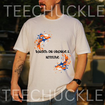 A man wearing a white graphic t-shirt with orange and blue paint splatters and the text 'RAISED ON GRUNGE & ATTITUDE'. The background is a blurred outdoor setting
