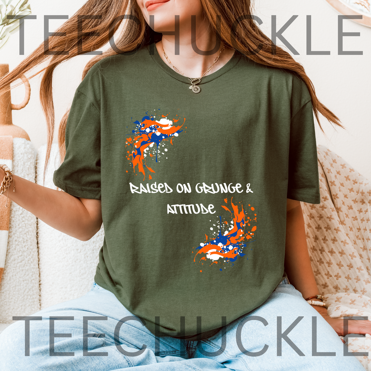 A woman wearing a green graphic t-shirt with orange and blue paint splatters and the text 'RAISED ON GRUNGE & ATTITUDE'.