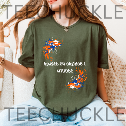A woman wearing a green graphic t-shirt with orange and blue paint splatters and the text 'RAISED ON GRUNGE & ATTITUDE'.
